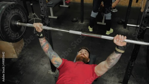 Young man lifting the barbell in the gym portrait. Steadycam follow shot of male athlete with brutal beard photo