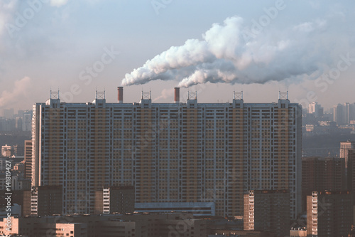 View from top of huge residential ship-like house with multiple regular windows and two big chimneys with smoke behind on sunny morning in residential district of metropolitan city