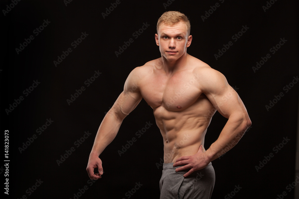 Athletic handsome man fitness-model showing six pack abs and oblique abdominal muscles. isolated on black background with copyspace