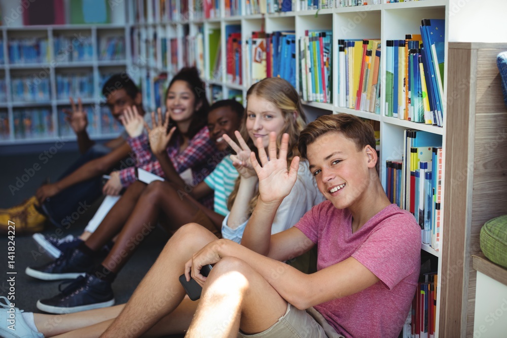 Fototapeta premium Students sitting in library and waving hands