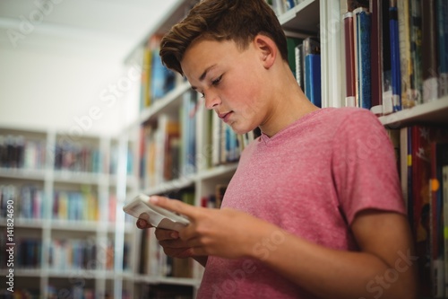 Happy schoolboy using digital tablet in library