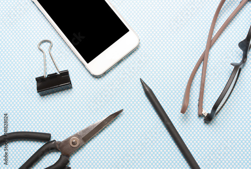 Phone, pen, pencil, glasses, scissors on a blue pea background .