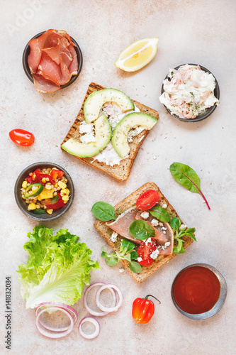 Open wholemeal sandwiches and various ingredients on rustic surface