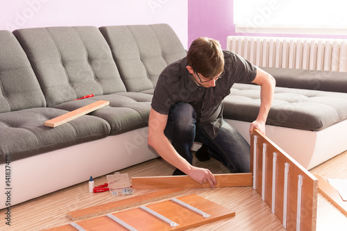 Picture how man made furniture in the living room. Hard work manager. Desperate man can not build a commode. Young man assembling furniture. Handyman building furniture in the living room.