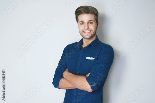 Portrait of happy smiling businessman in dark blue shirt crossing hands and looking at a camera. Business success concept