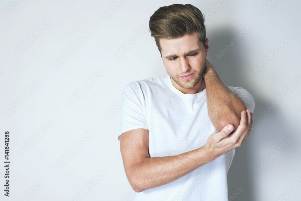 A young man in white t-shirt having pain in his injured elbow against grey background. Healthcare and medicine concept A young man in white t-shirt having pain in his injured elbow against grey background. Healthcare and medicine concept