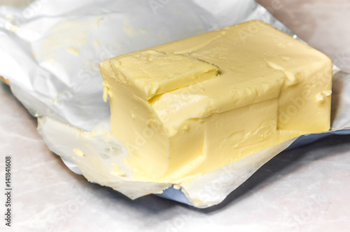 Creamy butter in its unwrapped foil paper. Isolated on light table