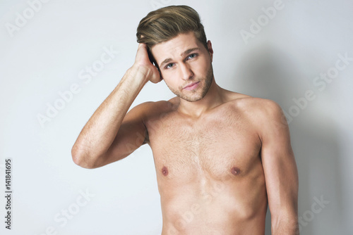 Perfect hairstyle and face. Smiling shirtless handsome man holding his arm on head and looking at camera against grey background. Portrait of charismatic man