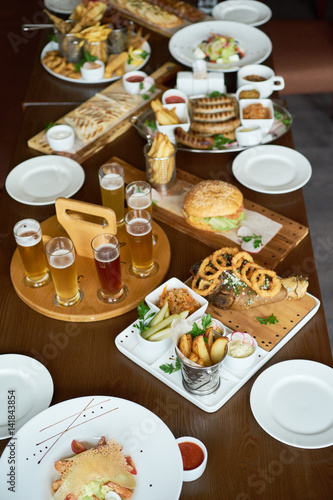 Photo Food set to beer slices and potato wedges with a beer glass on wooden backdrop, sausages and burger.