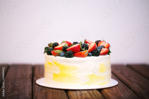 Birthday cake with strawberries, blueberries and blackberries on a dark wooden board