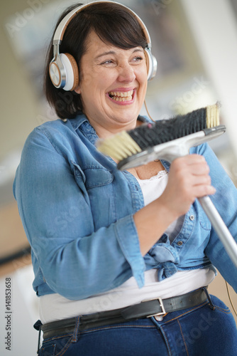 Tableau sur toile Cheerful overweigth woman having fun sweeping the floor