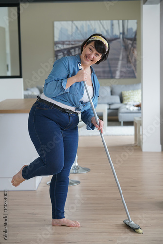 Cheerful overweigth woman having fun sweeping the floor