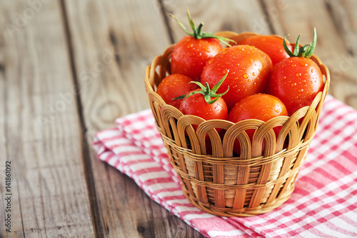 Fototapeta Naklejka Na Ścianę i Meble -  Fresh cherry tomatoes in woven basket on wooden background. Copy space