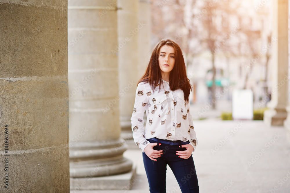 Fototapeta premium Young stylish brunette girl on shirt and pants posed near stone columns. Street fashion model concept.