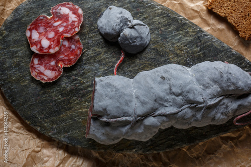 Sausage salami and knife on beige paper top and side view. Sausage sausage with ashes. French country sausage. Rustic food still life