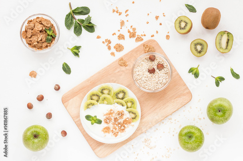 Healthy breakfast with yogurt, muesli, fresh green fruits, cereal, nuts on white background. Flat lay, top view.