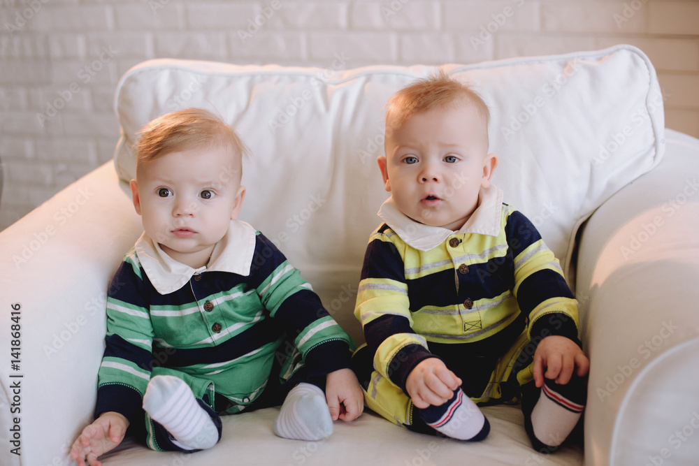 Two brother twins sitting. Two little kid boys watching at camera. Twins sitting together. People, children, friends and friendship concept Two brother twins sitting. Two little kid boys watching at camera. Twins sitting together. People, children, friends and friendship concept