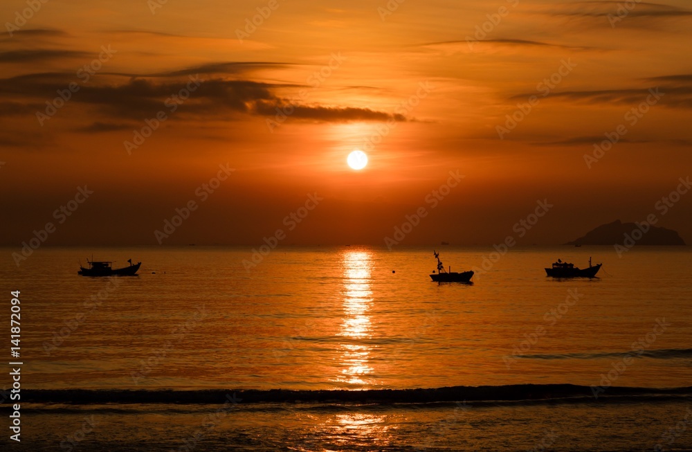 A fiery orange sunrise sky looking out over the south China sea in Vung Lam Bay Vietnam. With a fishing boats in silhouette.