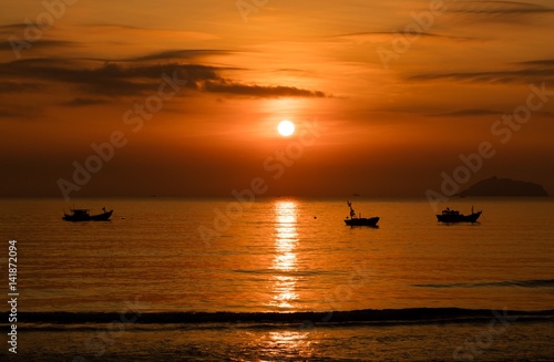 A fiery orange sunrise sky looking out over the south China sea in Vung Lam Bay Vietnam. With a fishing boats in silhouette. © Paul Hampton