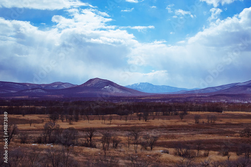 Picturesque countryside with arable lands, hills partially covered with snow in the foreground against the background of early spring.