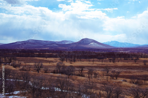 Picturesque countryside with arable lands  hills partially covered with snow in the foreground against the background of early spring.