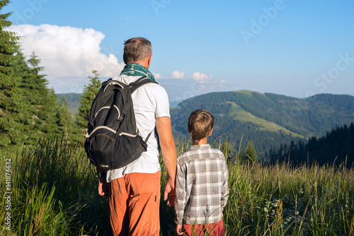 Father with son are standing on a alpine meadow among a lush grass