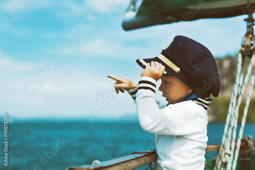 Konstfotografi Funny little baby captain on board of sailing yacht watching offshore sea on summer cruise