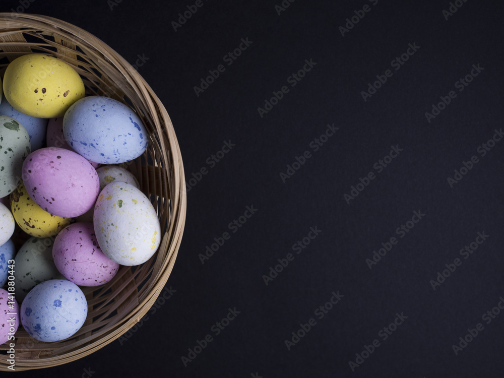 Easter chocolate eggs in pastel colors placed on small wooden basket and isolated on black background