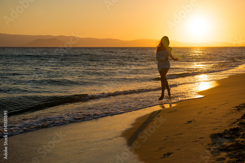 young girl is walking at sunset by the sea. Tourist girl on beach holiday. Happy girl running at sunset 