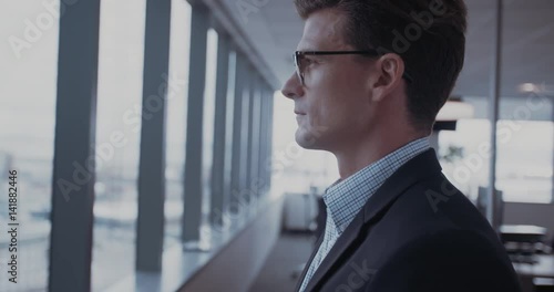 Side view shot of mature businessman standing in office and looking outside the window. Thooughtful entrepreneur in office looking at a view and smiling. photo