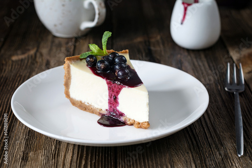 Obraz na płótnie Piece of cheesecake with black currant and blueberry sauce on white plate on woo