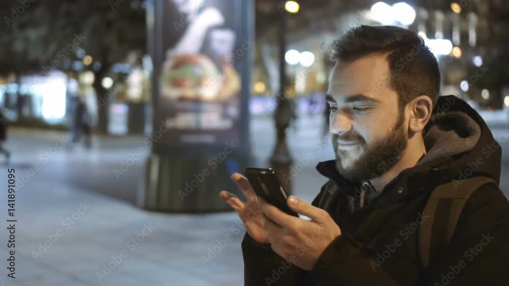 A young man is using his cellphone at night walking in a European city landmark or commercial street.100fps slow motion. A young man is using his cellphone at night walking in a European city landmark or commercial street.100fps slow motion.