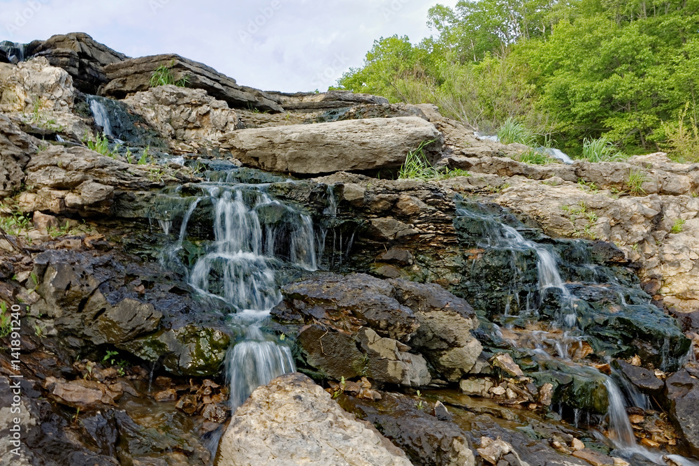 Fototapeta premium The water rushes over the Lake MacBride Waterfall. This waterfall has several main falls and numerous smaller falls.