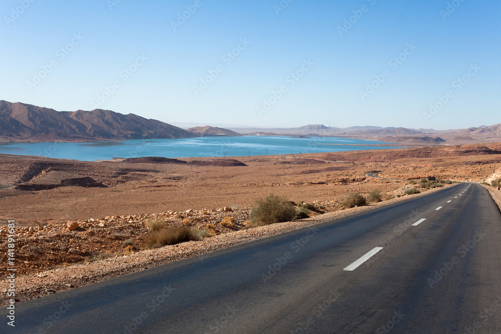 route droite au bord d'un lac au milieu d'un paysage aride