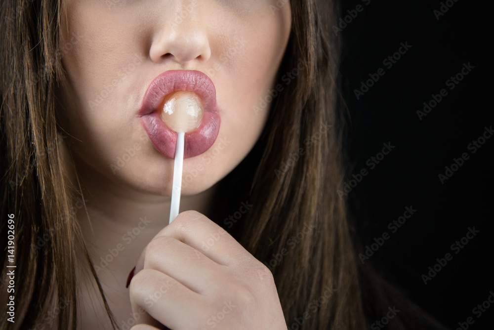 Juicy big lips of a young woman suck a lollipop, nice long fingers with red nail polish,isolated black background Juicy big lips of a young woman suck a lollipop, nice long fingers with red nail polish,isolated black background