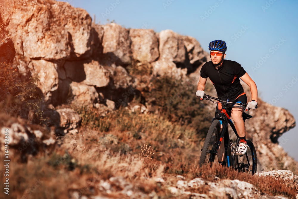 Cyclist in black sportwear Riding the Bike on the Rocky Trail. Extreme Sport Concept. Space for Text.
