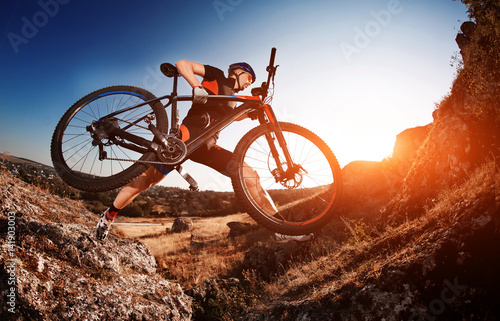 Professional Cyclist Taking his Bike up the Rocky Trail at evening. Extreme Sport Concept. Low angle and fisheye.