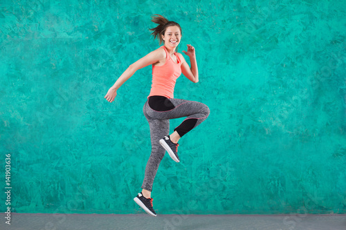 Sport young female in fashion sportswear jumping over turquoise background.