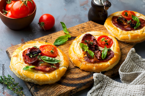 Mini tarts with dried meat, tomatoes, ricotta, thyme, basil and olives on a gray concrete background. Rustic style. Selective focus. photo