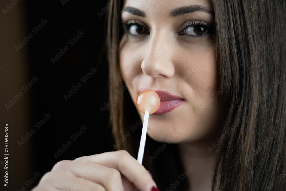 Young woman touching a lollipop on her juicy big lips, nice long thin finger with red nail polish,isolated black background Young woman touching a lollipop on her juicy big lips, nice long thin finger with red nail polish,isolated black background