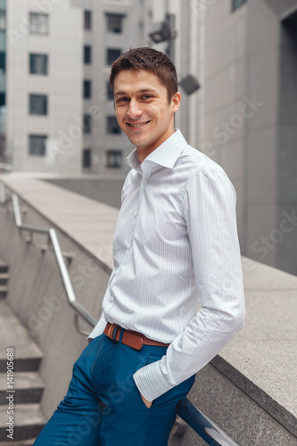Smiling businessman in formal wear standing outdoors with cityscape in the background. Looking at camera
