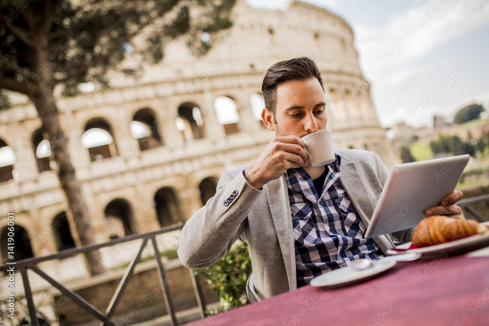 Fototapeta premium Young man sitting and having a cup of coffee in Rome, Italy