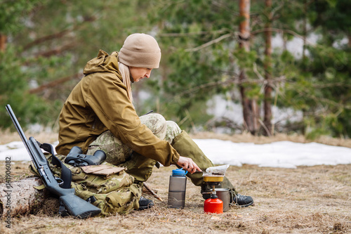 Female hunter preparing food with a portable gas burner in a winter forest.