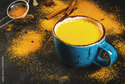 Traditional Indian drink turmeric milk is golden milk with cinnamon, cloves, pepper and turmeric. On a concrete table, with spices on the background. In mug, toned copy space