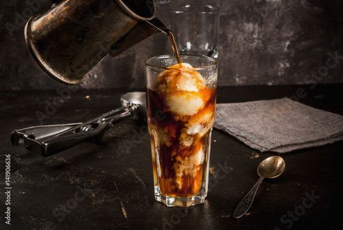 Cold coffee, frappe, frapuchchino. Affogato coffee with ice cream, On a concrete gray table. Toned, vintage. Coffee pot, spoon for ice cream, second glass. Smbd pours coffee into a glass, copy space