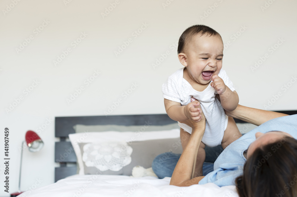 Cheerful baby boy playing with mother on bed at home Cheerful baby boy playing with mother on bed at home