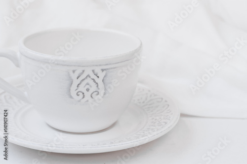 White relief ceramic tea cup with saucer on wood table cotton fabric, purity concept, minimalist, styled image for social media