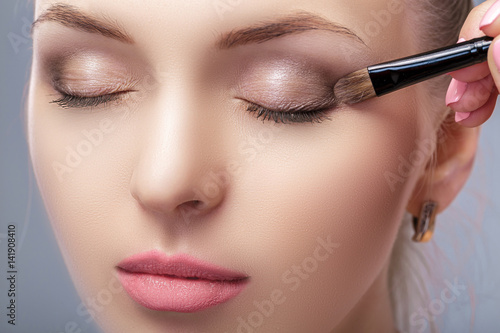 beautiful woman applying brown eye shadow using makeup brush. makeup for blue eyes photo