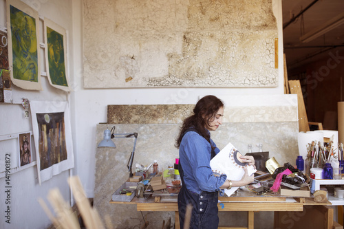 Side view of artist holding artwork by table in workshop