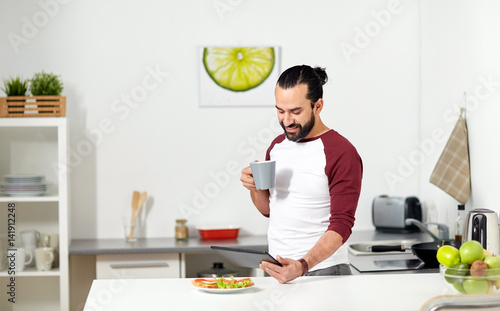 man with tablet pc eating at home kitchen